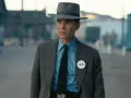 Julius Robert Oppenheimer w kapeluszu i garniturze, z odznaką K-6, w scenerii przypominającej miasteczko.