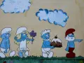 Smerfy z imionami: Papa Smerf wskazuje drogę, a kucharz niesie tort. Obok Smerfetka z kwiatkiem.