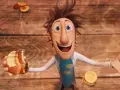 Flint Lockwood trzyma nadgryzionego hamburgera, podczas gdy wokół niego spadają klopsiki i inne zjawiska pogodowe.