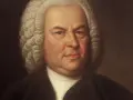 Portret Jana Sebastiana Bacha w peruce i stroju z epoki. Mistrz baroku spogląda z obrazu.