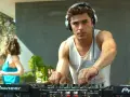 Zac Efron w filmach jako DJ na imprezie. W tle bawią się ludzie.