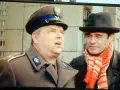Dwóch mężczyzn w kapeluszach, jeden w mundurze, drugi w szaliku. Brunet wieczorową porą, w czarnym kapeluszu i czerwonym szaliku, rozmawia z policjantem.