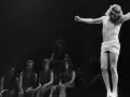 Scena z musicalu Jesus Christ Superstar: Jezus na krzyżu, otoczony przez postaci, w tym kobiety siedzące wpatrzone w niego.