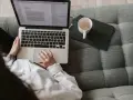 Kobieta pisze na laptopie, zastanawiając się, ile zarabia scenarzysta. Obok kubek i tablet.