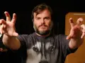 Jack Black w koszulce z wilkiem, z wyciągniętymi rękami. Ciekawe, ile lat ma Jack Black, gdy tak energicznie gestykuluje?