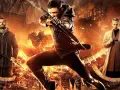 Robin Hood początek: młody łucznik w akcji, obok mężczyźni z toporem i w płaszczu, w tle płonące ruiny i konie.