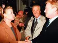Monika Dzienisiewicz-Olbrychska w brązowym płaszczu wita się z mężczyznami. W tle widać kamery i innych ludzi.