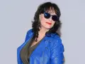 Anna Maria Korcz w niebieskiej ramonesce i okularach przeciwsłonecznych, z czerwoną szminką na ustach.