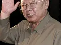 Kim Jong Il w okularach, machający ręką.