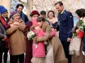 Rodzina w zimowych płaszczach i czapkach, z bukietami kwiatów, tworzy radosny tłum. Może to być scena z filmu, gdzie piszą list do Świętego Mikołaja.