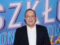 Uśmiechnięty mężczyzna w okularach na tle napisu "SZKŁO KONTAKTOWE". Prowadzący wydarzenie, gotowy do rozmowy.