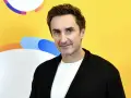 Sebastian Karpiel Bułecka w białej koszulce i czarnym kardiganie na tle żółtej ściany z kolorowymi elementami.