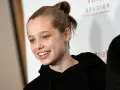 Uśmiechnięta Shiloh Jolie Pitt z włosami upiętymi w kok, w czarnej bluzie z kapturem.