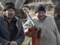 Dwóch rolników z Podlasia, w czapkach i ciepłych ubraniach, przy maszynie rolniczej.