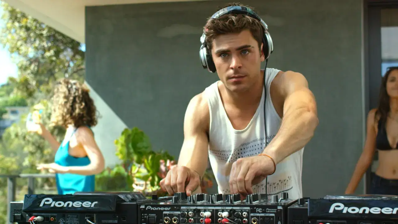 Zac Efron w filmach jako DJ na imprezie. W tle bawią się ludzie.