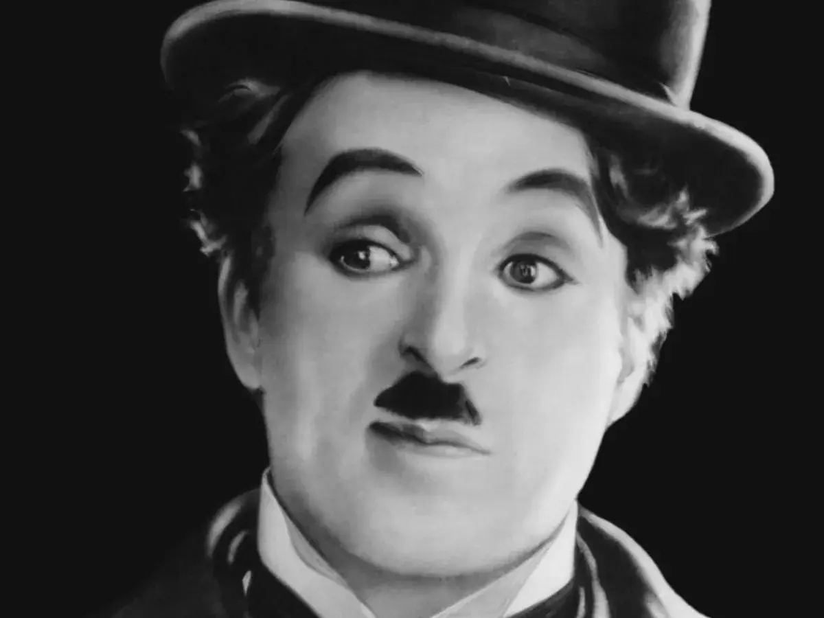 Charlie Chaplin w meloniku, z charakterystycznym wąsikiem, jakby opowiadał historie dla dzieci.