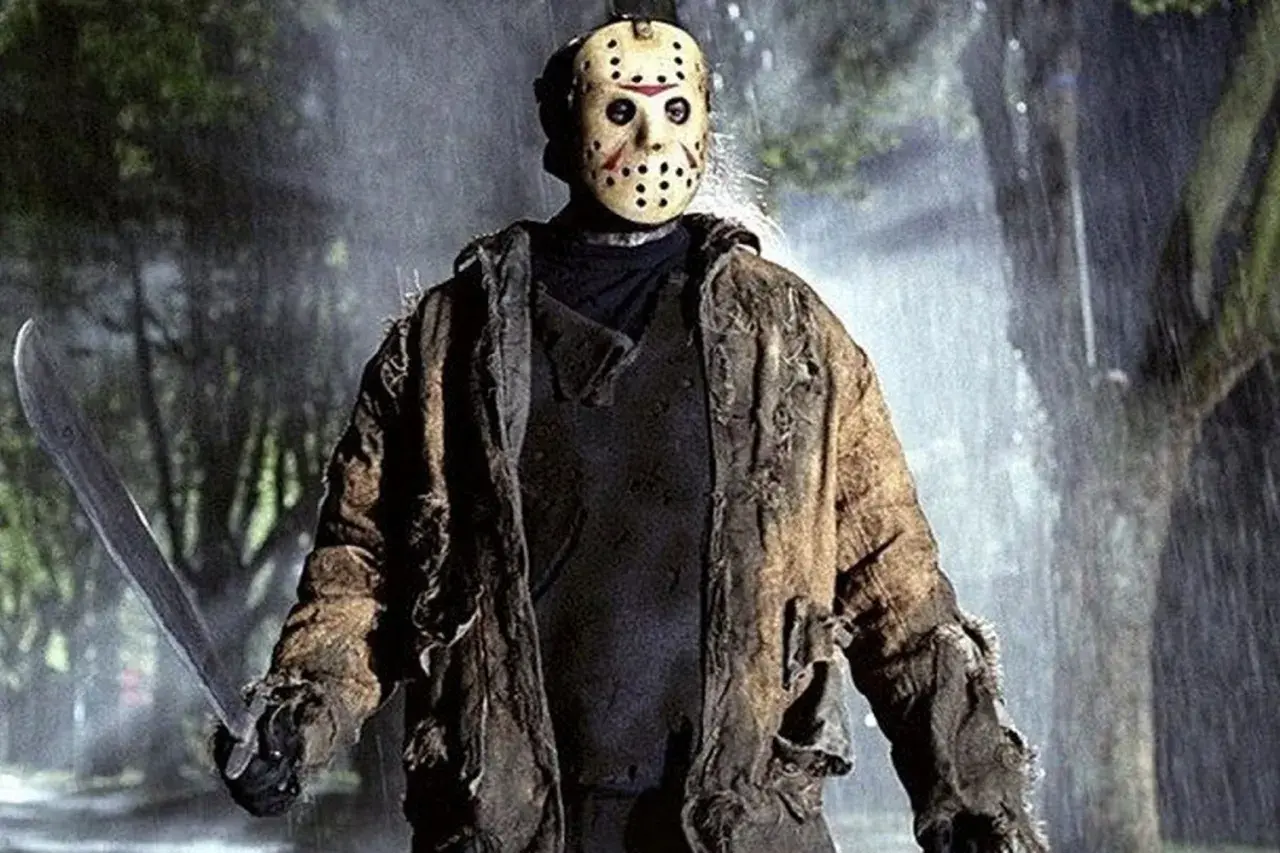 Jason Voorhees, ikona horrorów, w swojej zniszczonej kurtce i z maczetą, stoi w deszczu.