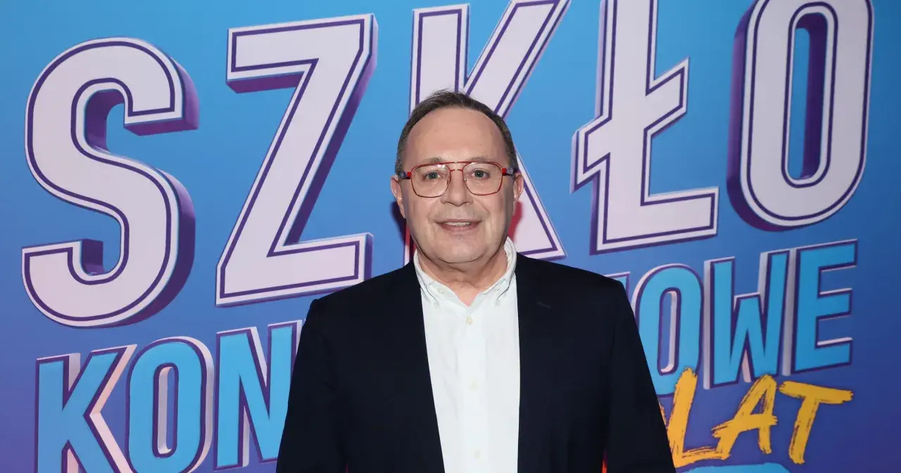 Uśmiechnięty mężczyzna w okularach na tle napisu "SZKŁO KONTAKTOWE". Prowadzący wydarzenie, gotowy do rozmowy.