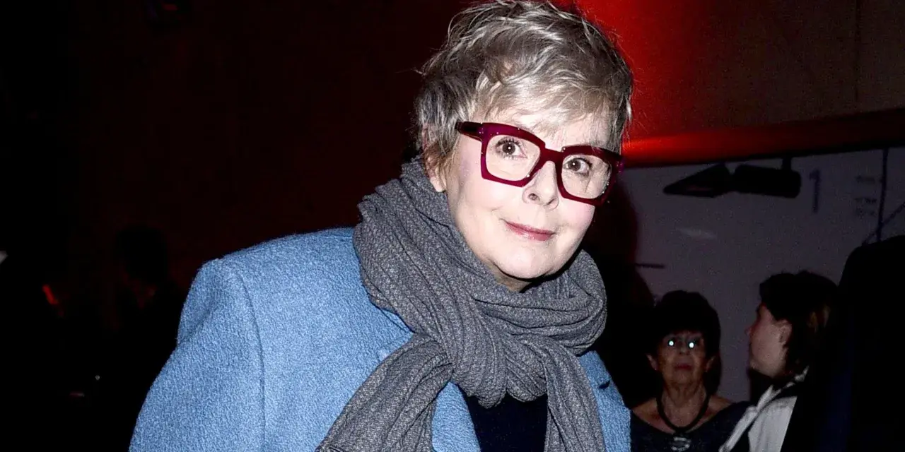 Karolina Korwin Piotrowska w okularach i niebieskim płaszczu, z szarym szalem na szyi.