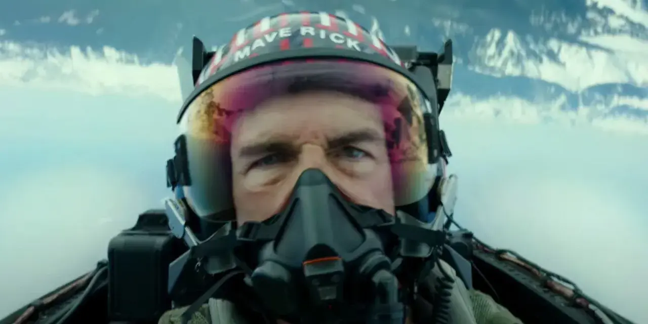 Tom Cruise jako Maverick w hełmie z napisem "MAVERICK" w filmie Top Gun: Maverick. Intensywne spojrzenie pilota w kokpicie myśliwca.