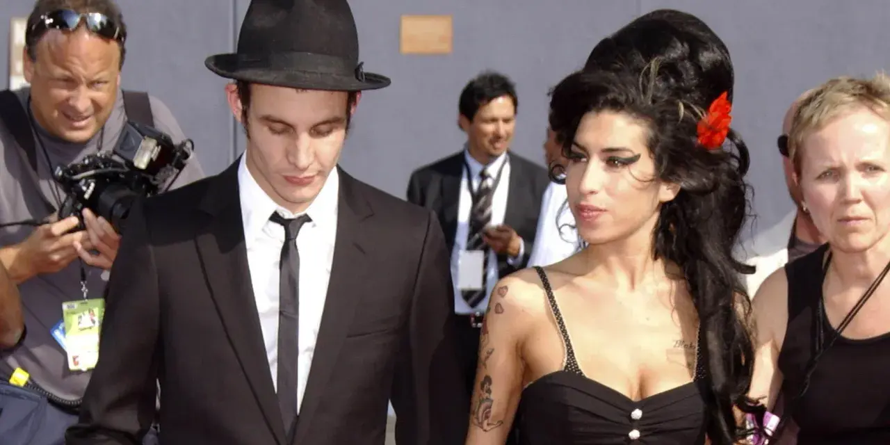 Blake Fielder-Civil w czarnym garniturze i kapeluszu obok Amy Winehouse z czerwoną różą we włosach.