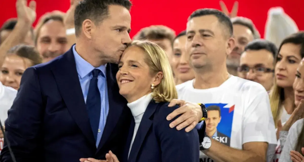 Rafał Trzaskowski, choć nie znamy jego dokładnego wieku, czule całuje żonę na tle tłumu.