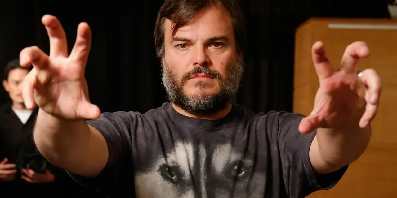 Jack Black w koszulce z wilkiem, z wyciągniętymi rękami. Ciekawe, ile lat ma Jack Black, gdy tak energicznie gestykuluje?