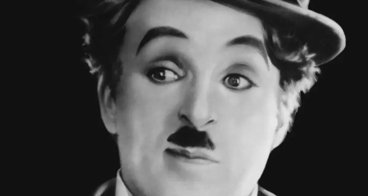 Charlie Chaplin w meloniku, z charakterystycznym wąsikiem, jakby opowiadał historie dla dzieci.