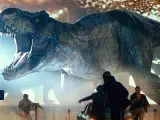 Gigantyczny Tyranozaur Rex z Jurassic World 3 z otwartą paszczą ściga ludzi wśród samochodów.