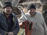 Dwóch rolników z Podlasia, w czapkach i ciepłych ubraniach, przy maszynie rolniczej.