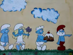 Smerfy z imionami: Papa Smerf wskazuje drogę, a kucharz niesie tort. Obok Smerfetka z kwiatkiem.