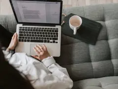 Kobieta pisze na laptopie, zastanawiając się, ile zarabia scenarzysta. Obok kubek i tablet.