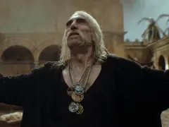 Leo Bonhart, z długimi siwymi włosami i wąsami, w czarnym ubraniu, z kilkoma medalionami na szyi, stoi na deszczu.