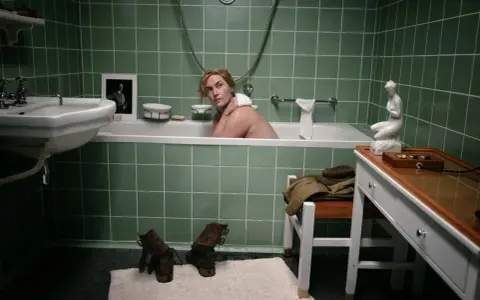Kobieta w wannie, obok zdjęcie mężczyzny w mundurze. Buty i ubrania na podłodze. Zobacz to lee na własne oczy.