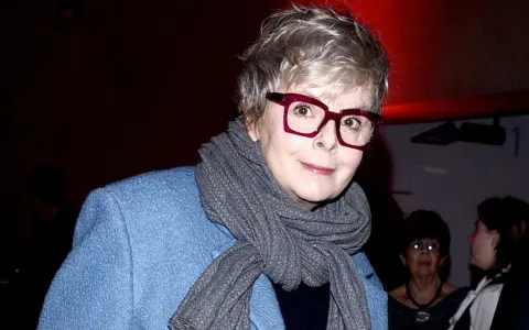 Karolina Korwin Piotrowska w okularach i niebieskim płaszczu, z szarym szalem na szyi.