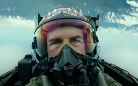 Tom Cruise jako Maverick w hełmie z napisem "MAVERICK" w filmie Top Gun: Maverick. Intensywne spojrzenie pilota w kokpicie myśliwca.