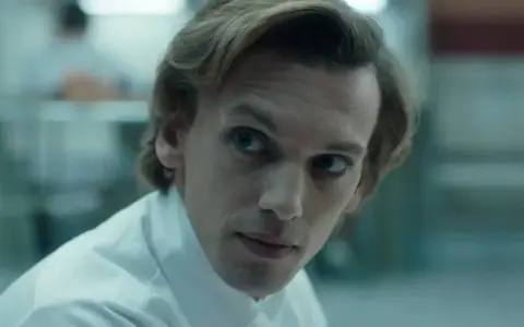 Henry Creel, znany jako Vecna z 001 stranger things, w białej koszuli, patrzy z uwagą.