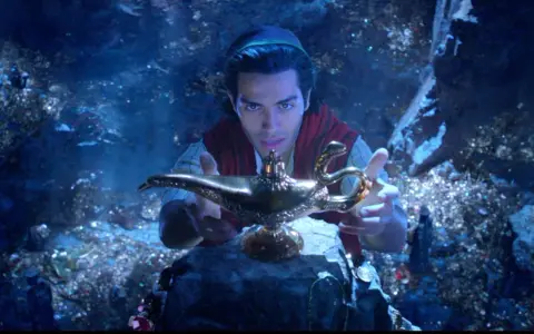 Aladyn, w mrocznej jaskini pełnej skarbów, trzymając magiczną lampę.