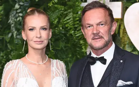Cezary Pazura z żoną Edytą na ściance. Ona w białej, zdobionej sukni, on w eleganckim garniturze.