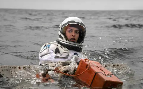 Astronautka w skafandrze z filmu Interstellar 2 w wodzie, z pomarańczowym urządzeniem.