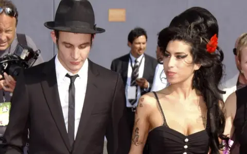 Blake Fielder-Civil w czarnym garniturze i kapeluszu obok Amy Winehouse z czerwoną różą we włosach.