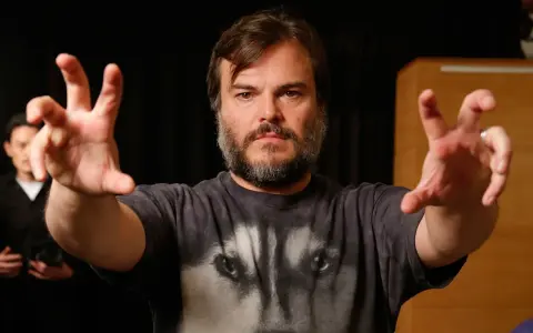 Jack Black w koszulce z wilkiem, z wyciągniętymi rękami. Ciekawe, ile lat ma Jack Black, gdy tak energicznie gestykuluje?