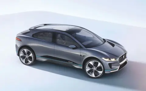Elegancki, szary Jaguar I-PACE, niczym czarny jaguar gotowy do skoku, prezentuje swoją aerodynamiczną sylwetkę na jasnym tle.
