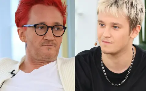 Xavier Michał Wiśniewski z charakterystycznymi rudymi włosami i okularami obok młodszego mężczyzny z blond fryzurą.