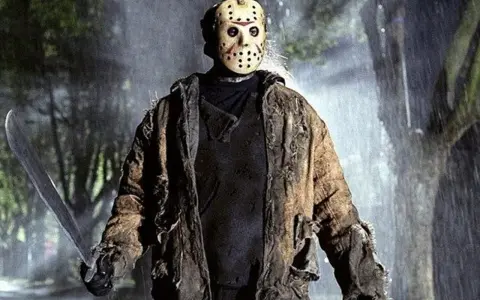 Jason Voorhees, ikona horrorów, w swojej zniszczonej kurtce i z maczetą, stoi w deszczu.