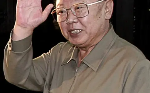 Kim Jong Il w okularach, machający ręką.