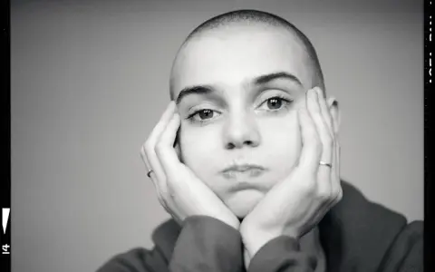 Sinead O'Connor z dłońmi opartymi o policzki, zamyślona.