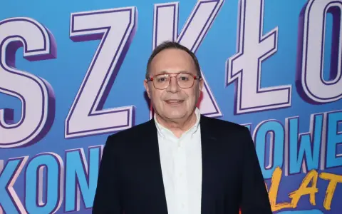 Uśmiechnięty mężczyzna w okularach na tle napisu "SZKŁO KONTAKTOWE". Prowadzący wydarzenie, gotowy do rozmowy.
