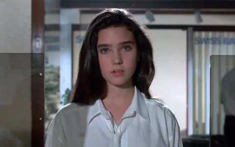 Młoda Jennifer Connelly w białej koszuli, z charakterystycznym spojrzeniem, jak z jej wczesnych filmów.
