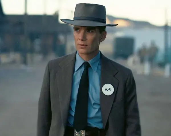 Julius Robert Oppenheimer w kapeluszu i garniturze, z odznaką K-6, w scenerii przypominającej miasteczko.